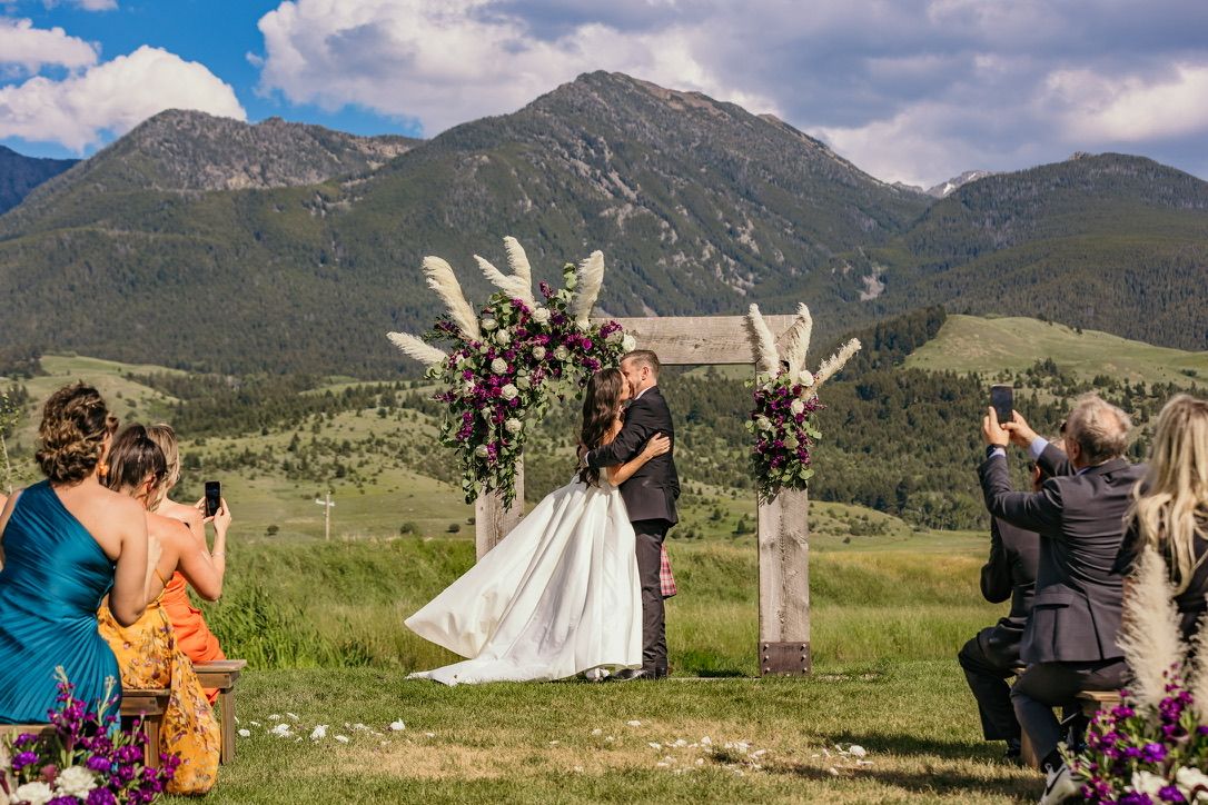 Outdoor wedding ceremony with floral arch against mountain landscape.