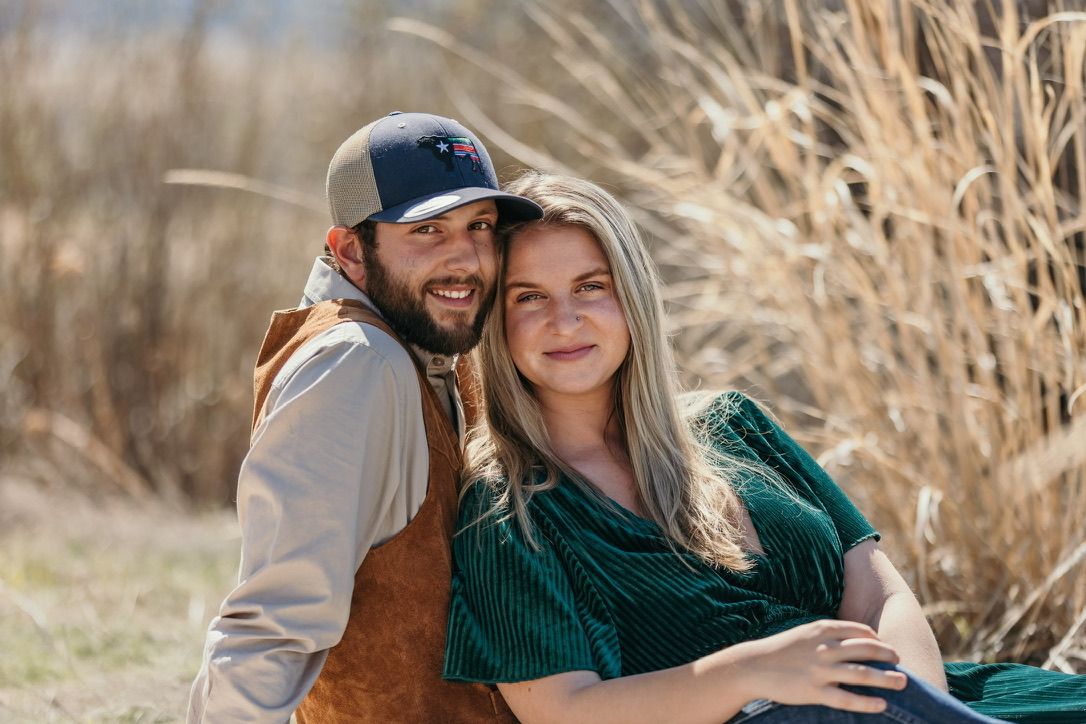 A couple shares an intimate moment while posing together near tall dried grasses.