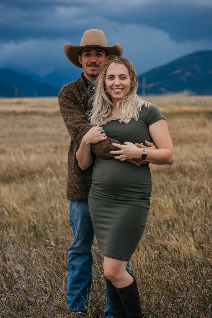 A couple poses together in a field with mountains behind them during golden hour.