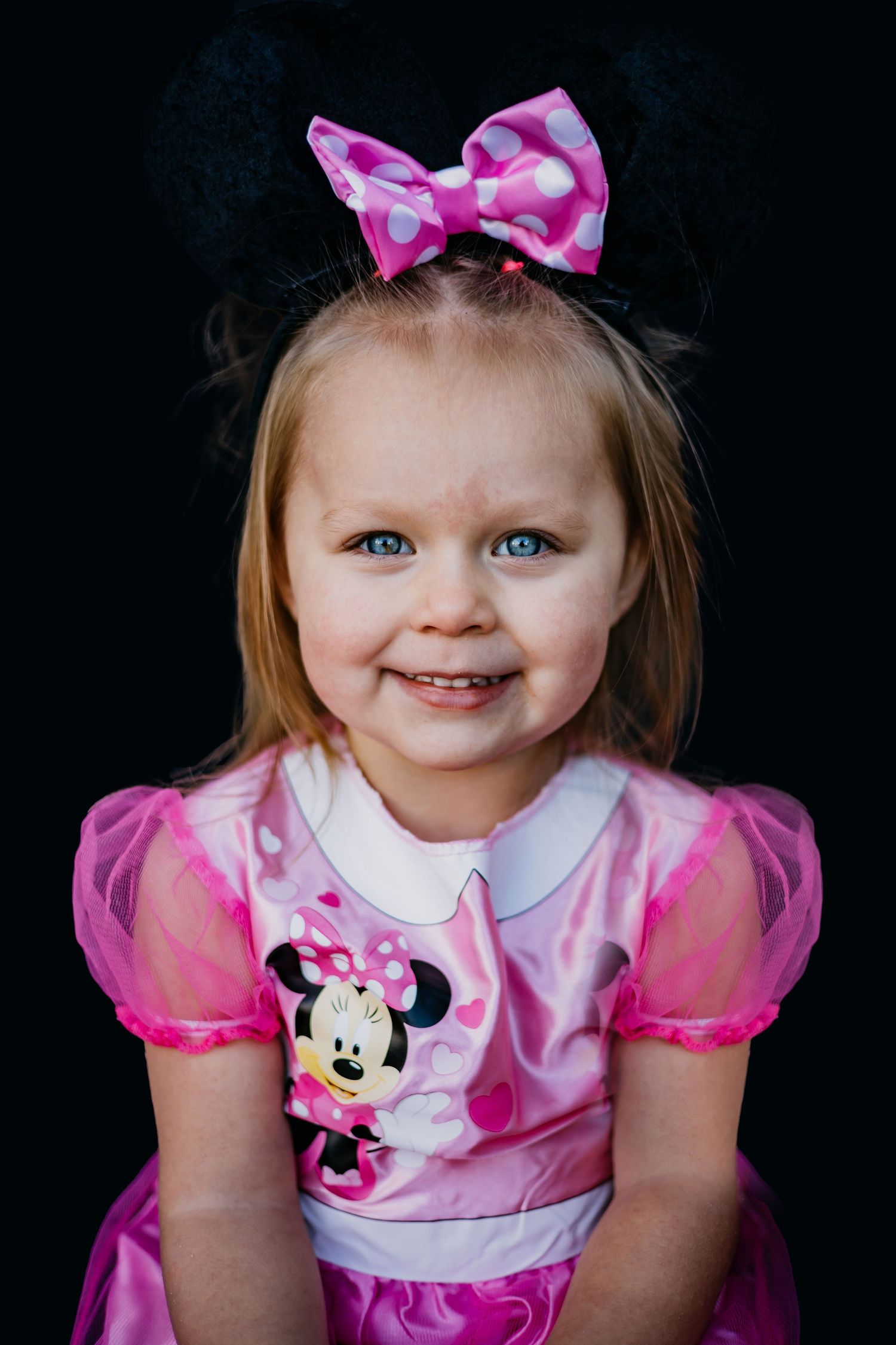 Adorable pink Minnie Mouse dress costume with matching bow against dark background.