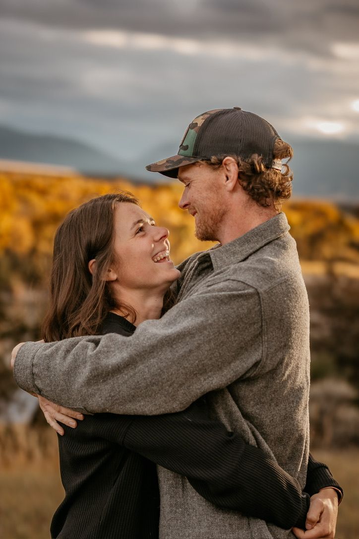 Couple embracing and laughing during golden hour with desert landscape behind them.