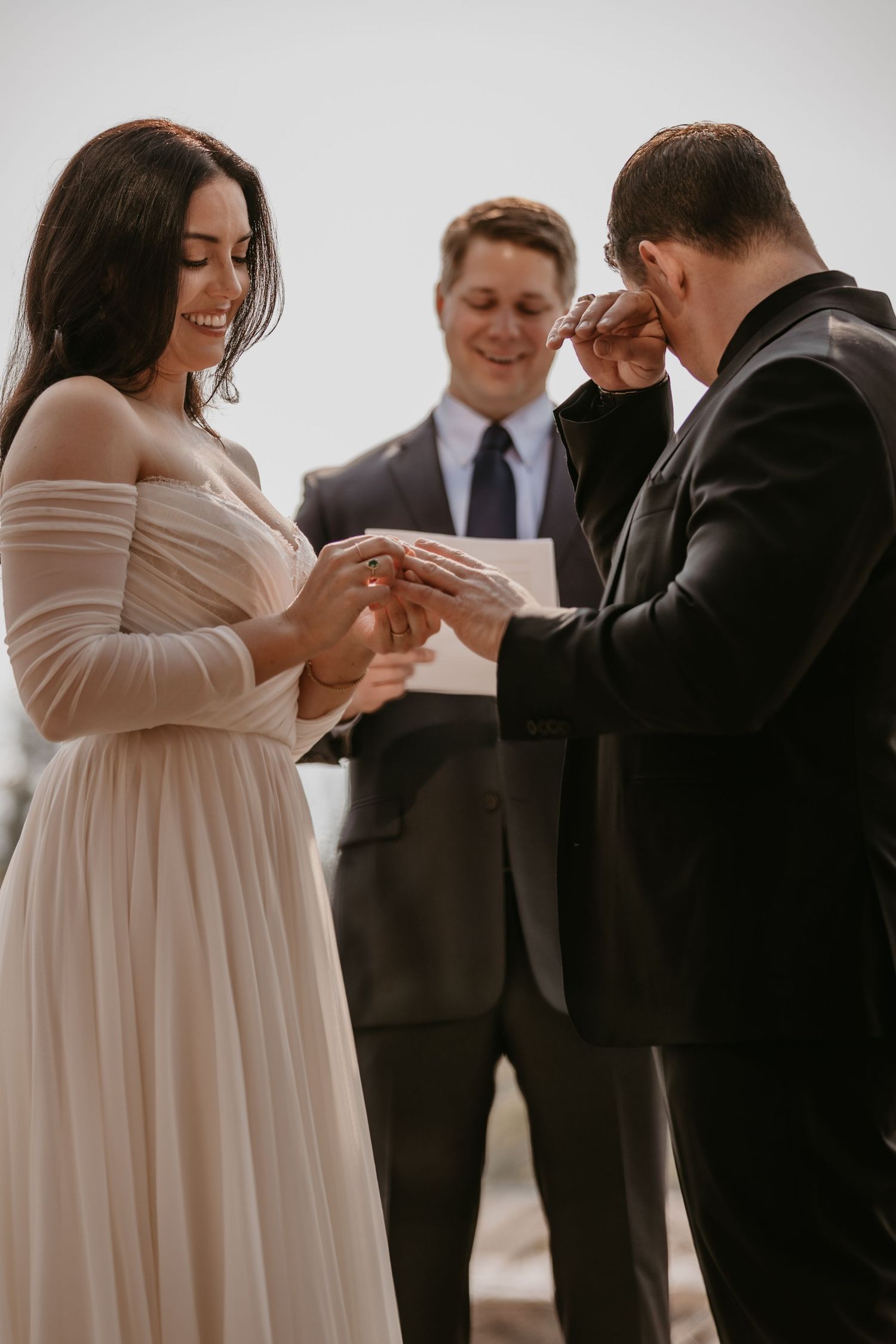 A couple exchanges rings during their wedding ceremony with an officiant present.