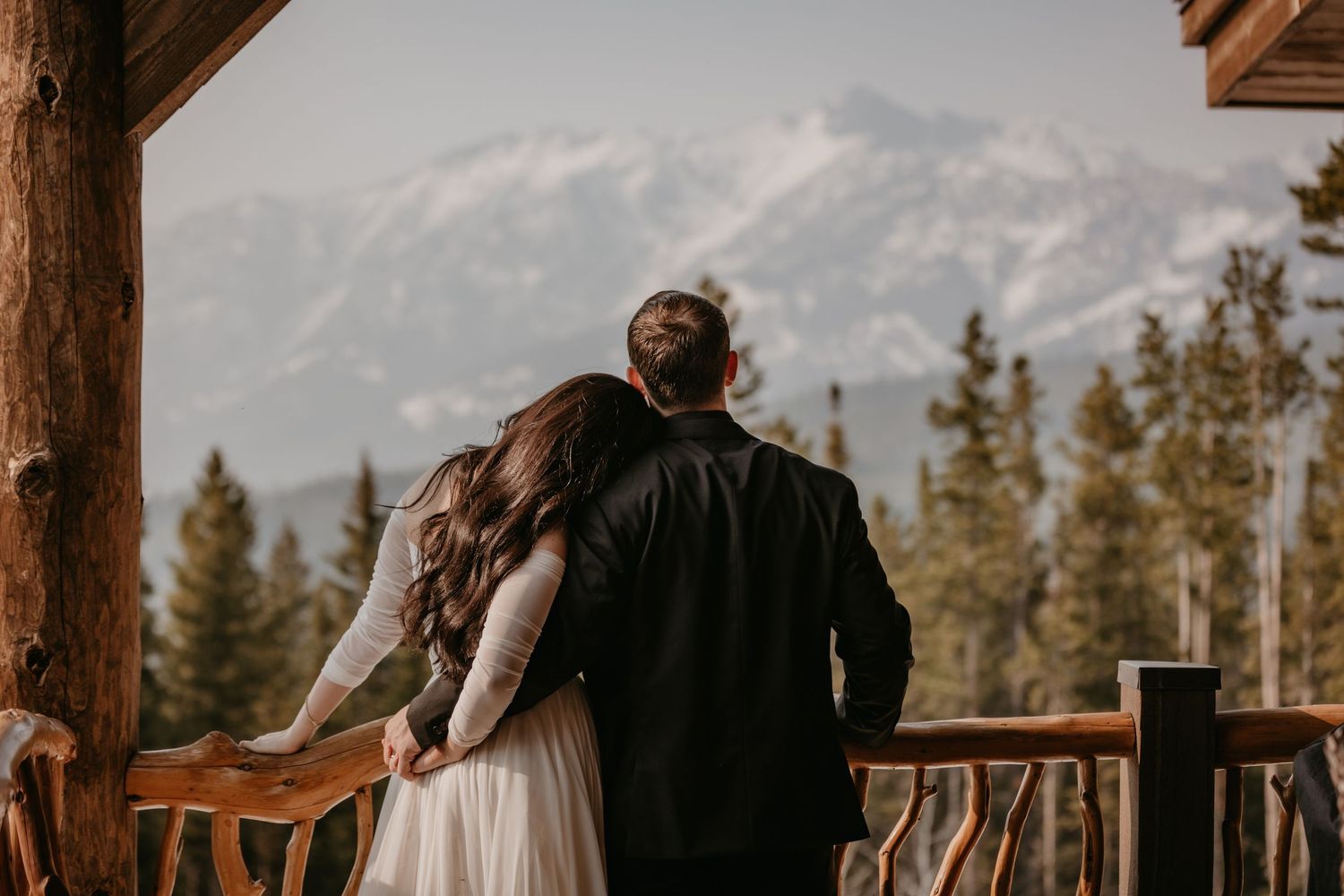 Newlyweds enjoying romantic moments on a mountain lodge deck with forest views.