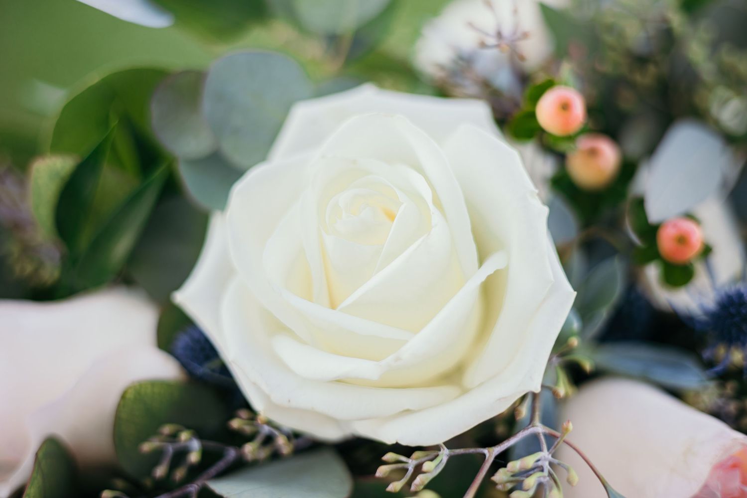 Delicate white roses and pink buds arranged with greenery and berries in an elegant wedding floral display.
