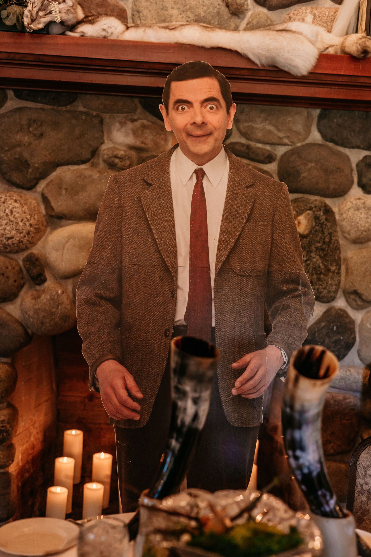 Man in brown tweed suit poses with candles in rustic stone room setting.
