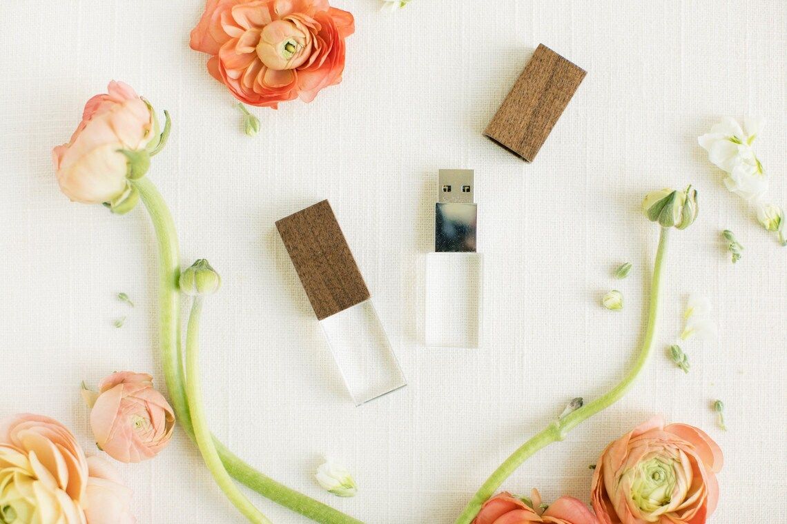 Wooden USB drives arranged with peach ranunculus flowers and white floral accents on a white background.