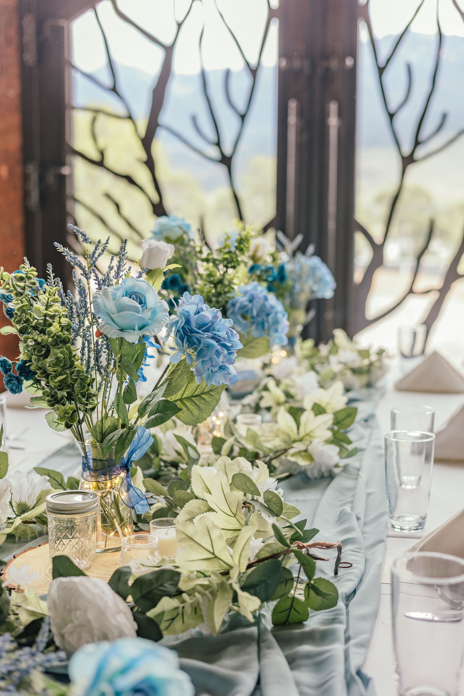 Elegant blue and white floral table centerpieces with greenery in mason jars.