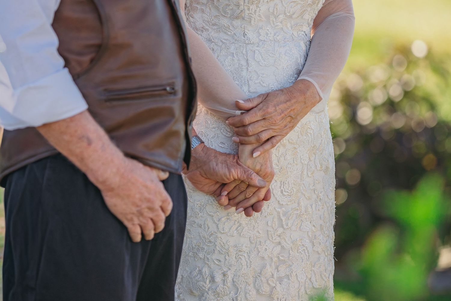 Elegant lace wedding dress details shown during outdoor ceremony.