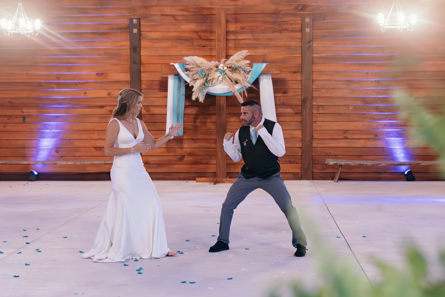 Couple performs playful dance moves during wedding reception on wooden floor.