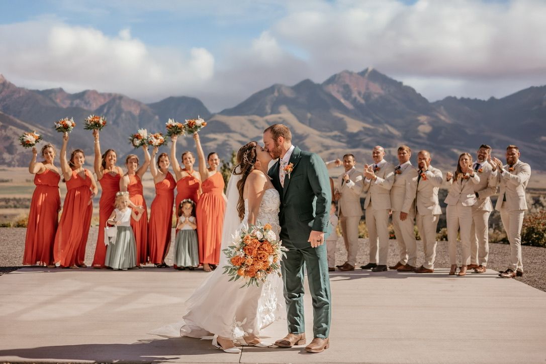 Large wedding party in coral and beige attire posed against desert mountain landscape.