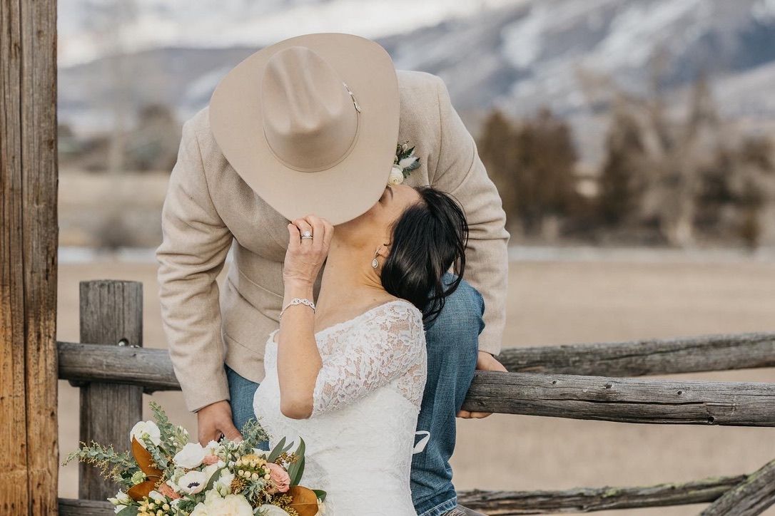 Rustic wooden fence frames couple's wedding photos against mountain scenery.