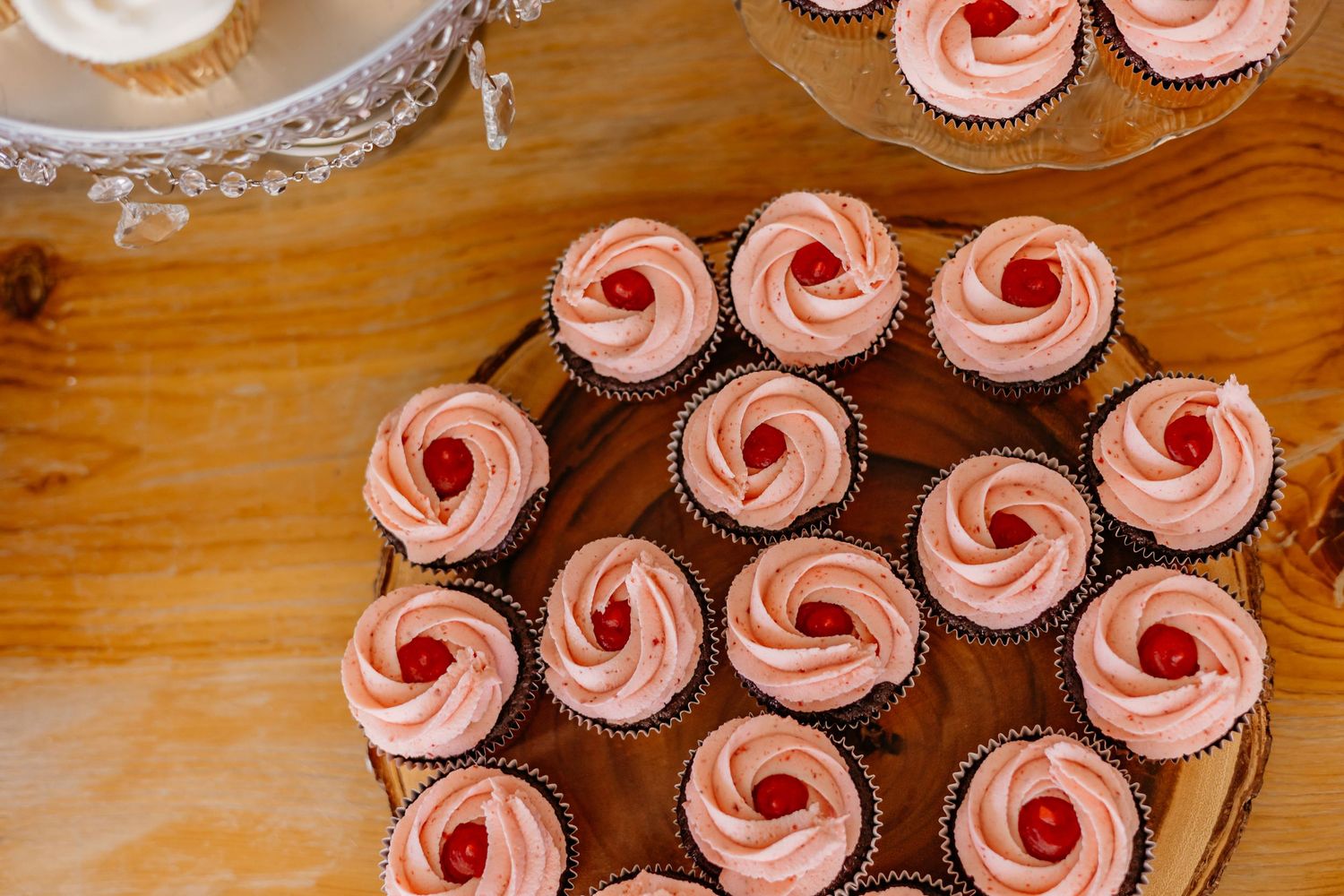 Pink frosted cupcakes with red cherry toppings displayed in rows for an event.