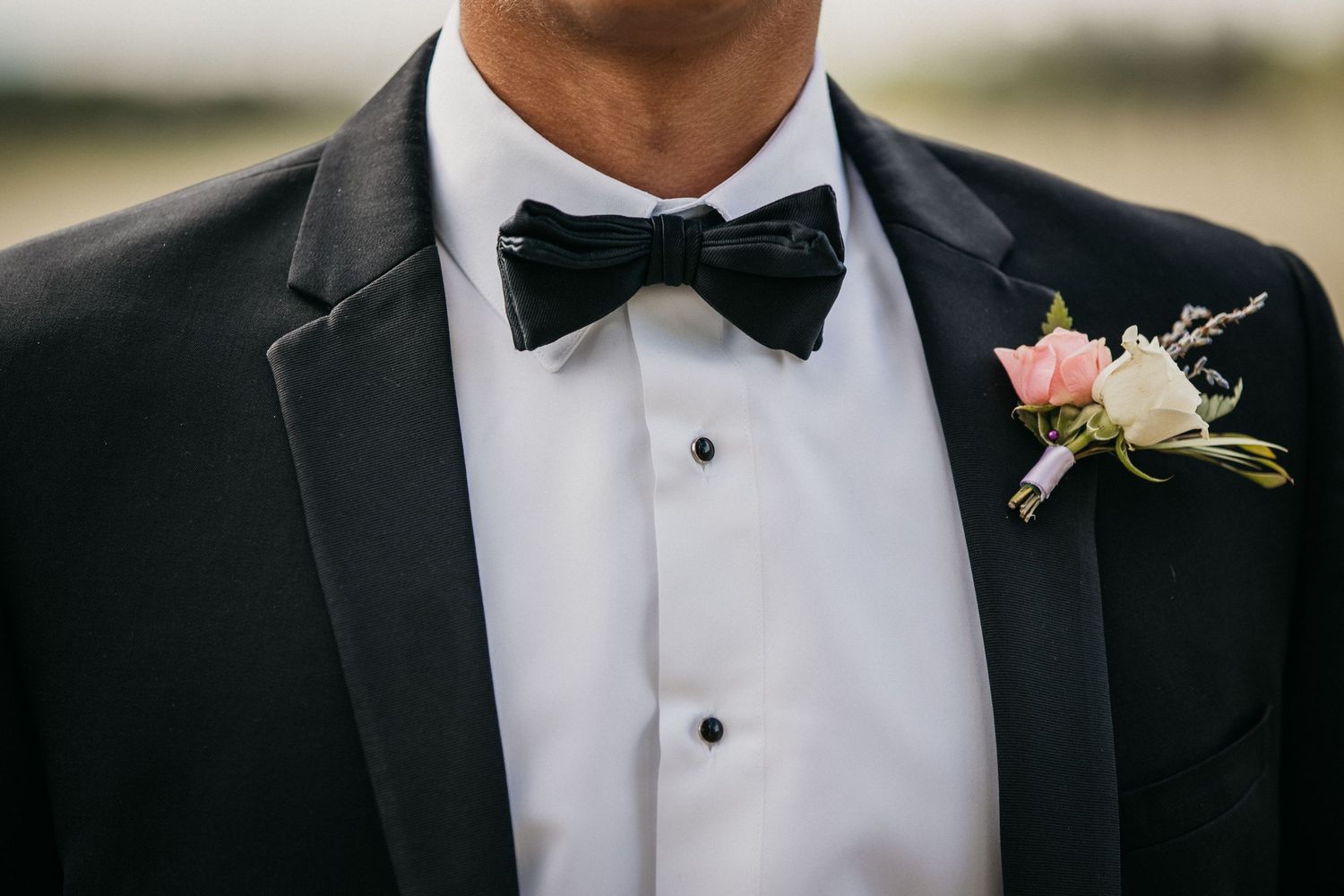 Close-up details of formal black tuxedos with bow ties and boutonnières.