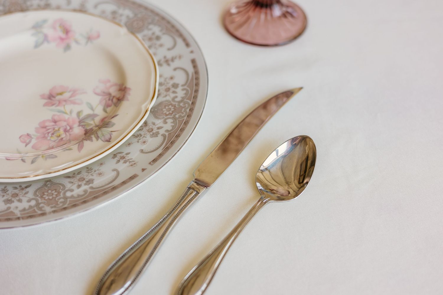 Vintage floral china plates and silverware arranged on white linen tablecloth.