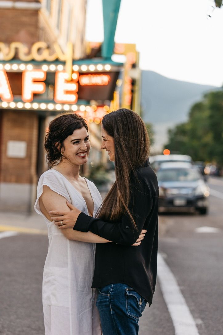 Couple embracing on street with vintage cafe sign and lights in background.