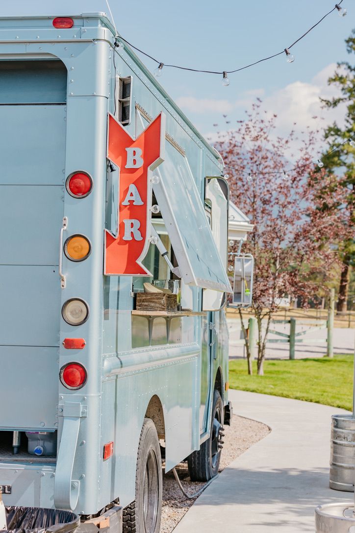 Vintage blue food truck with red bar sign parked in sunny outdoor setting.