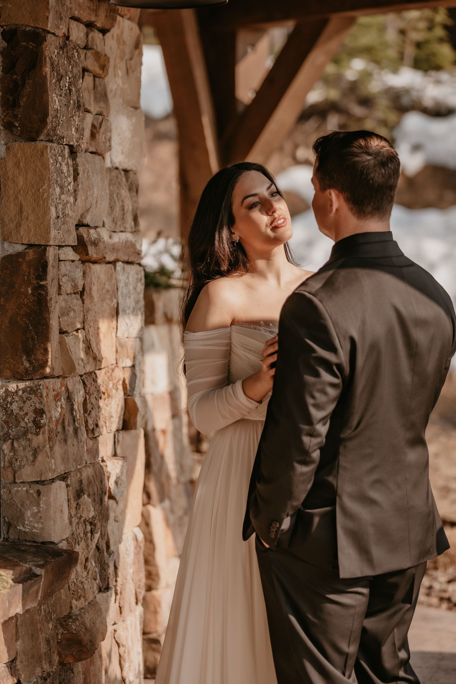 Romantic wedding couple poses between stone pillars in warm lighting.