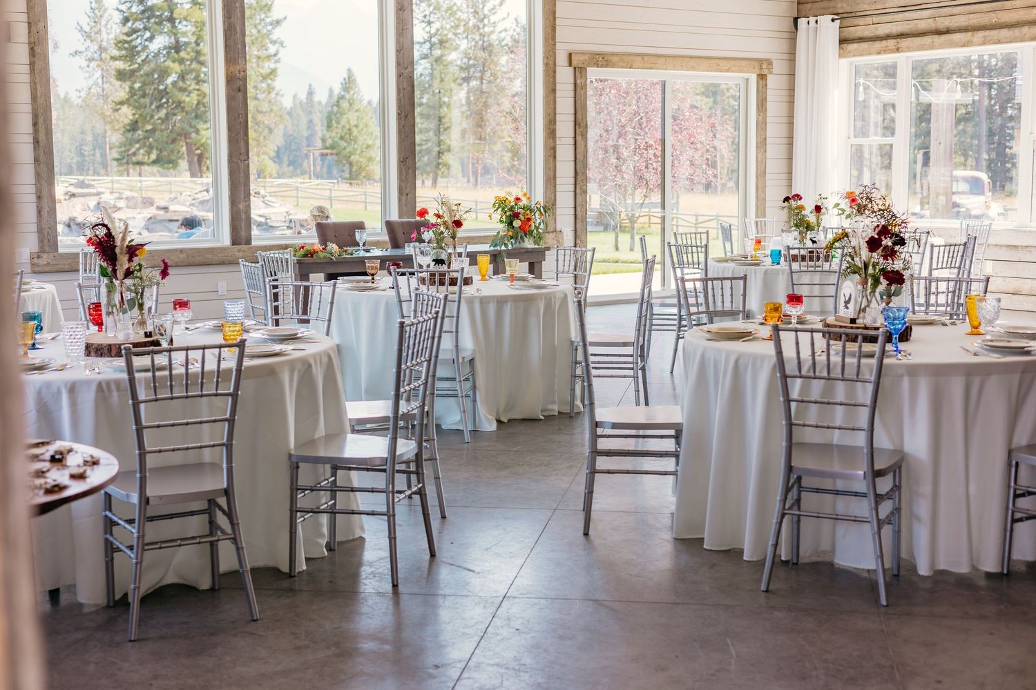 Spacious reception venue with white-clothed tables and chairs arranged in an airy, window-lined room.