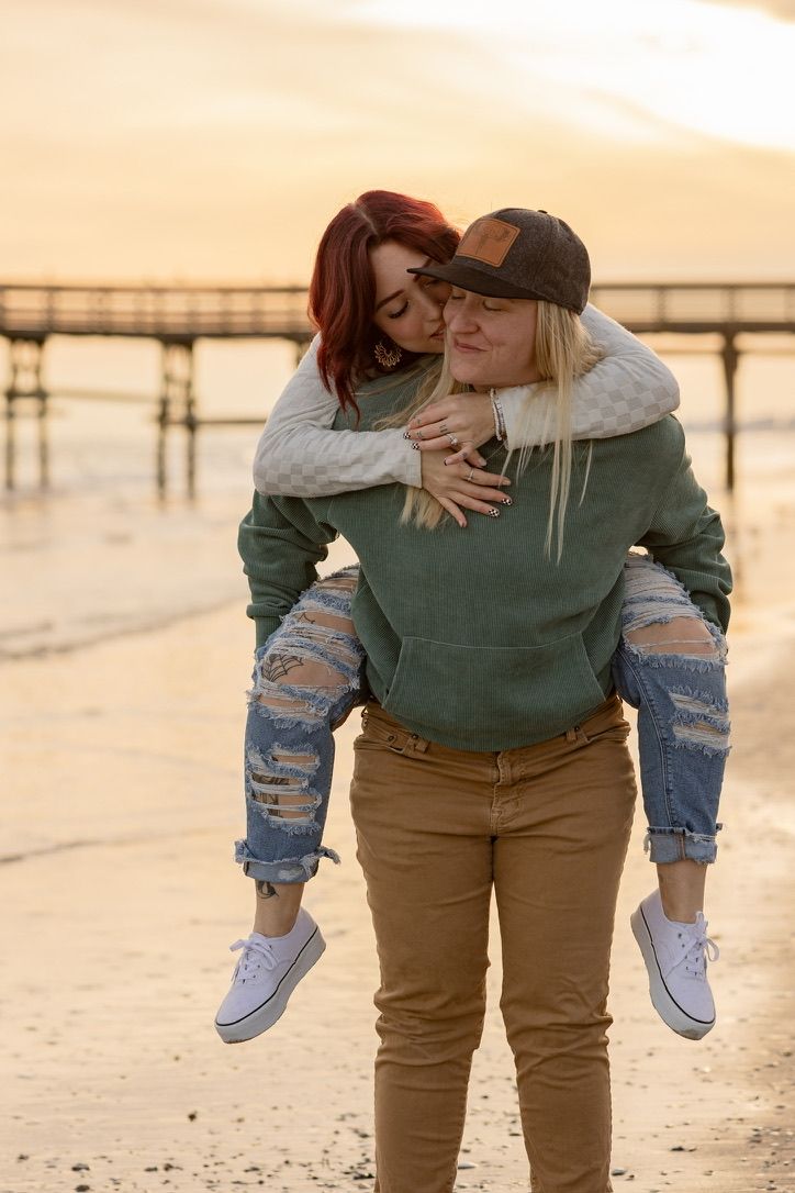A playful couple shares a piggyback ride on the beach at sunset.