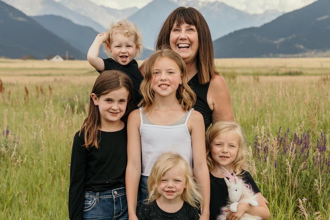 Family gathering outdoors with mountain peaks and green fields in the background.
