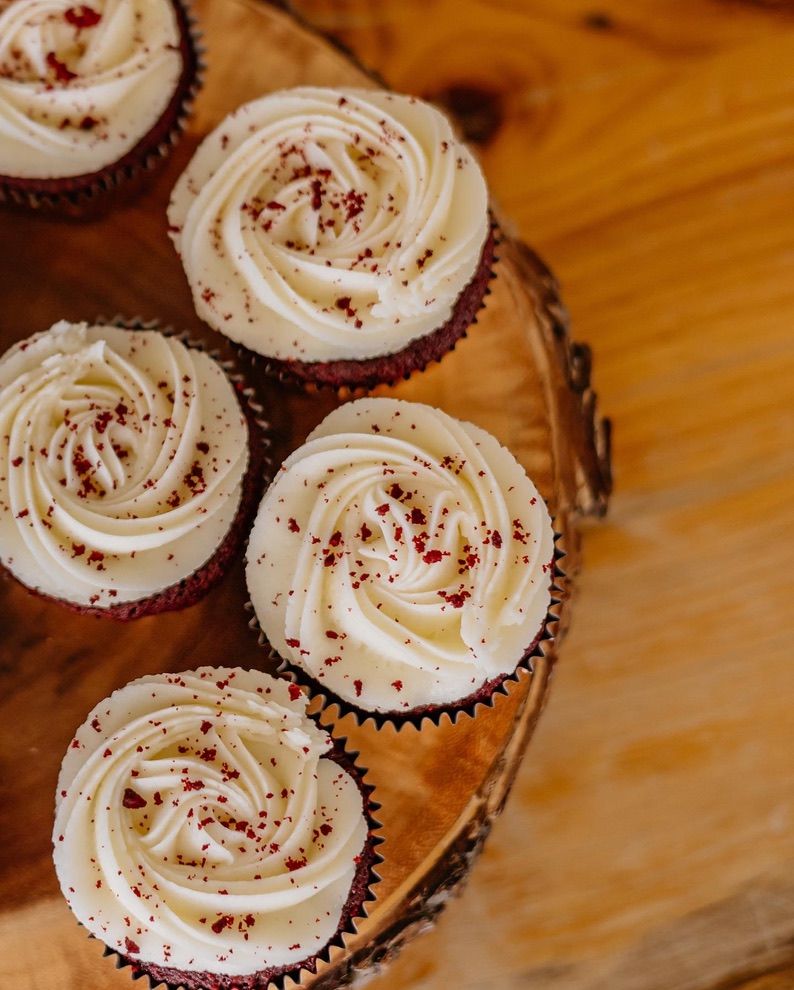 Chocolate cupcakes topped with swirled white frosting and red sprinkles displayed on a wooden surface.