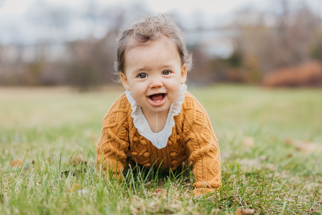 Baby in mustard colored outfit crawling on grass during autumn photo session.