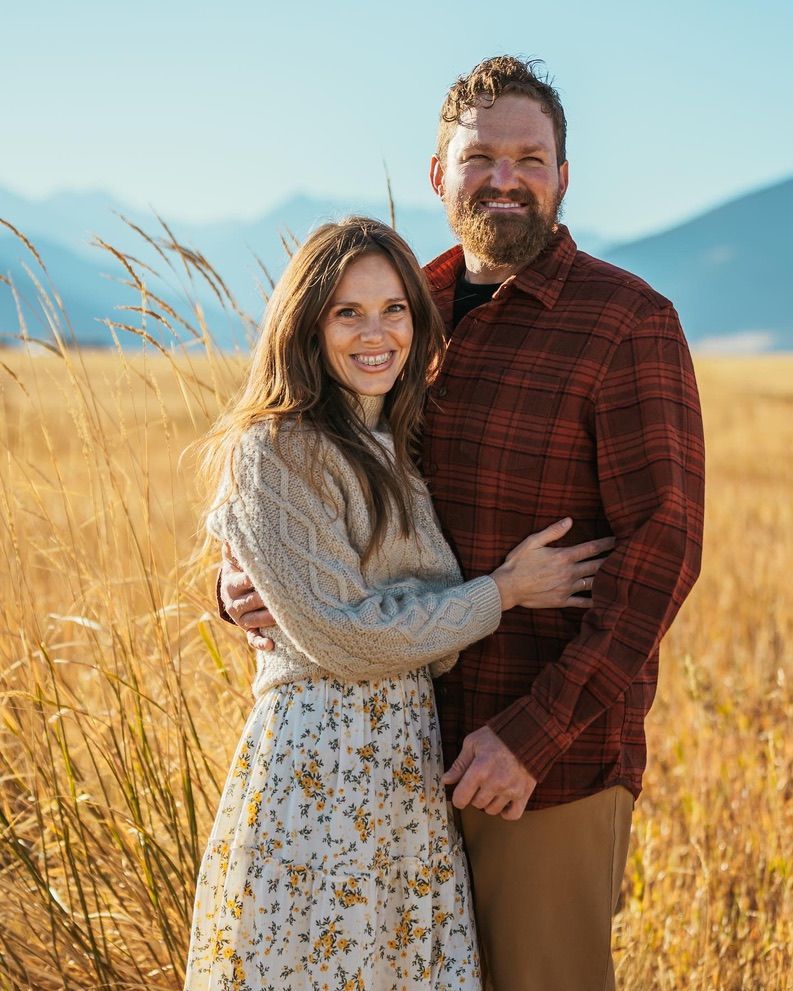 Couple embracing in golden field with mountains and autumn colors.