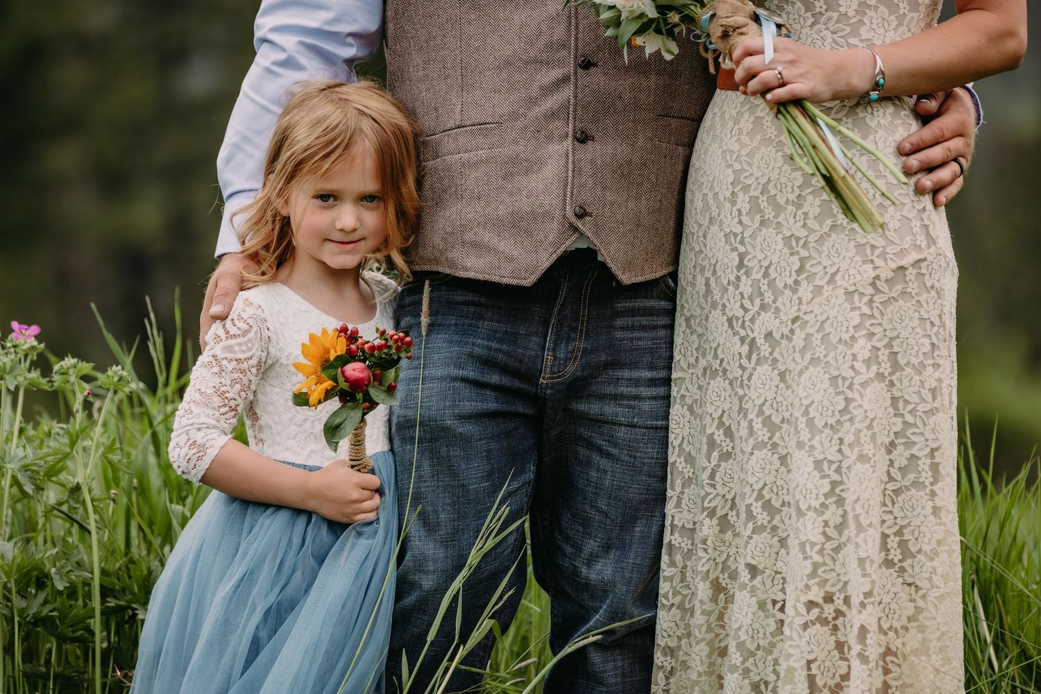 Wedding party members in casual attire holding bouquets against natural outdoor setting.