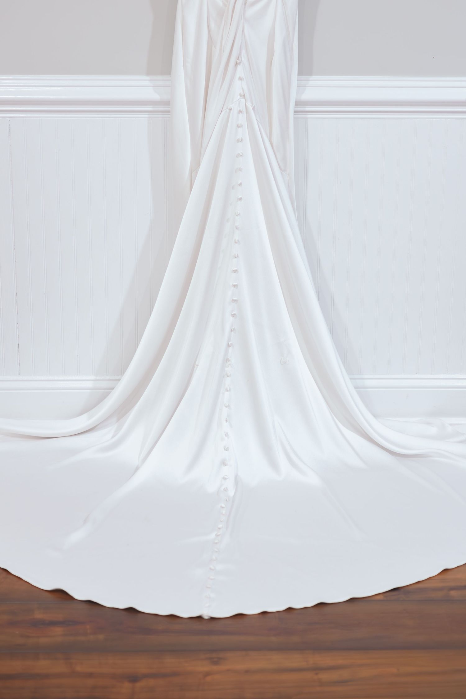 Close-up details of a white wedding dress train flowing across wooden floor.