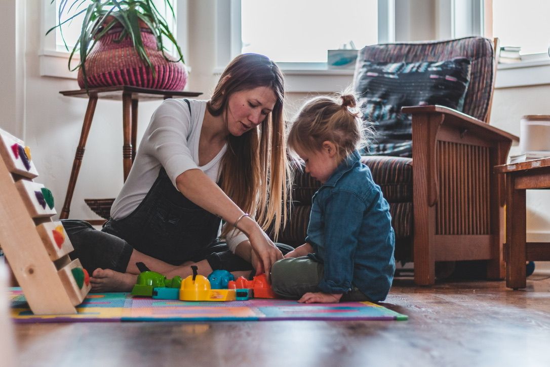 Parent and child playing with colorful building blocks on floor at home.
