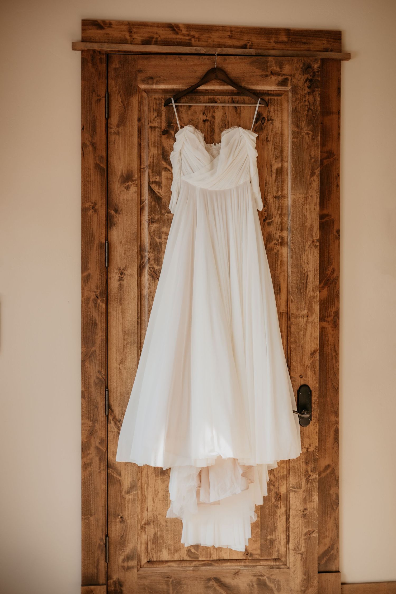 A white wedding dress hanging on a wooden rustic door.
