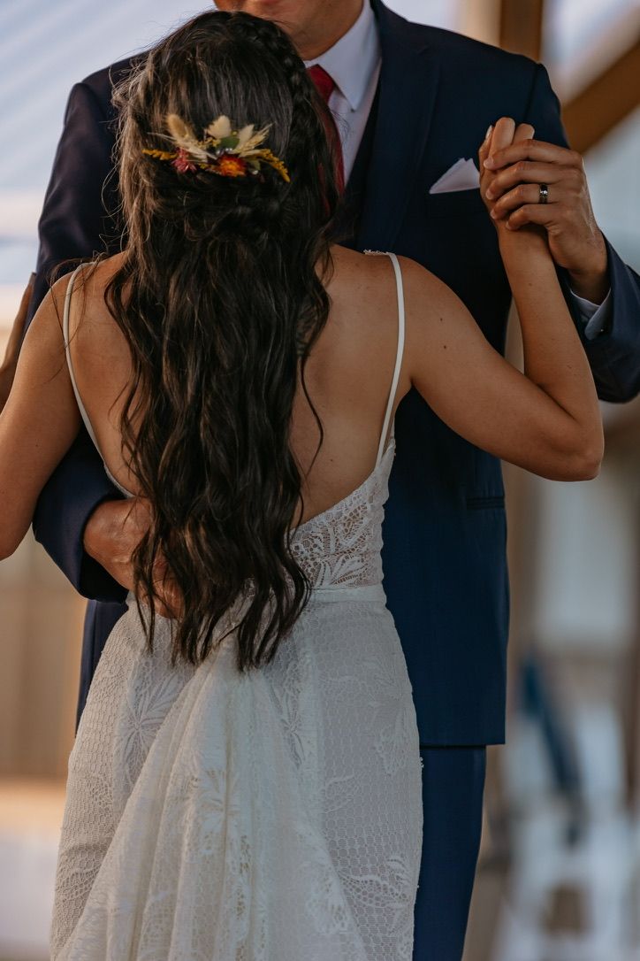 Bride in a white lace dress and groom in navy suit pose together during their wedding photoshoot.