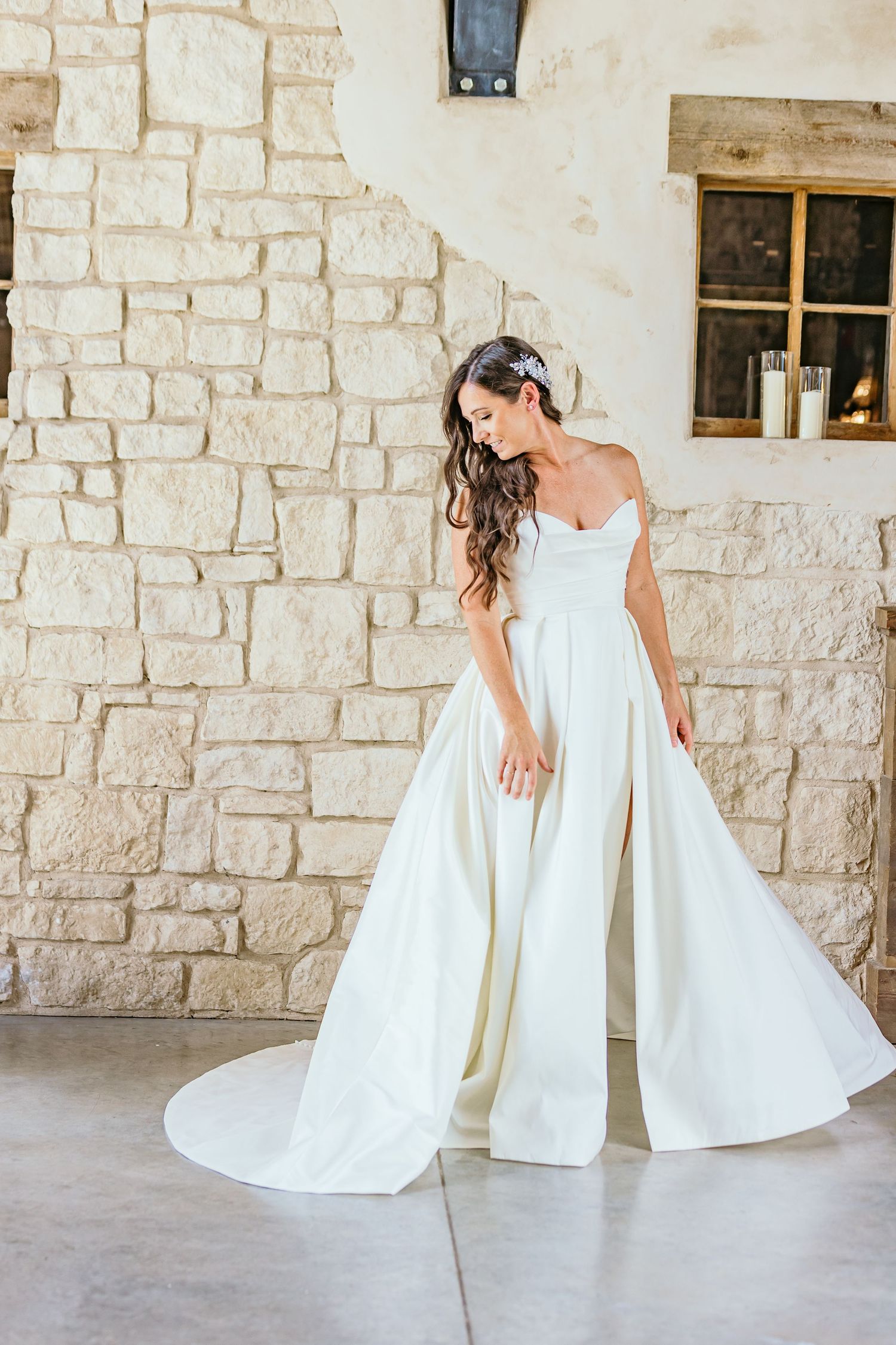 An elegant white wedding gown with a sweetheart neckline twirls against a stone wall exterior.