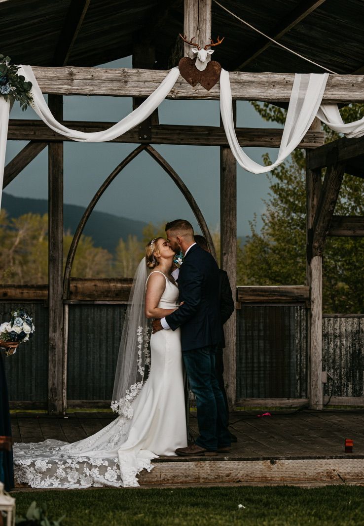 Outdoor wedding ceremony under draped white fabric and arched windows with mountain views.