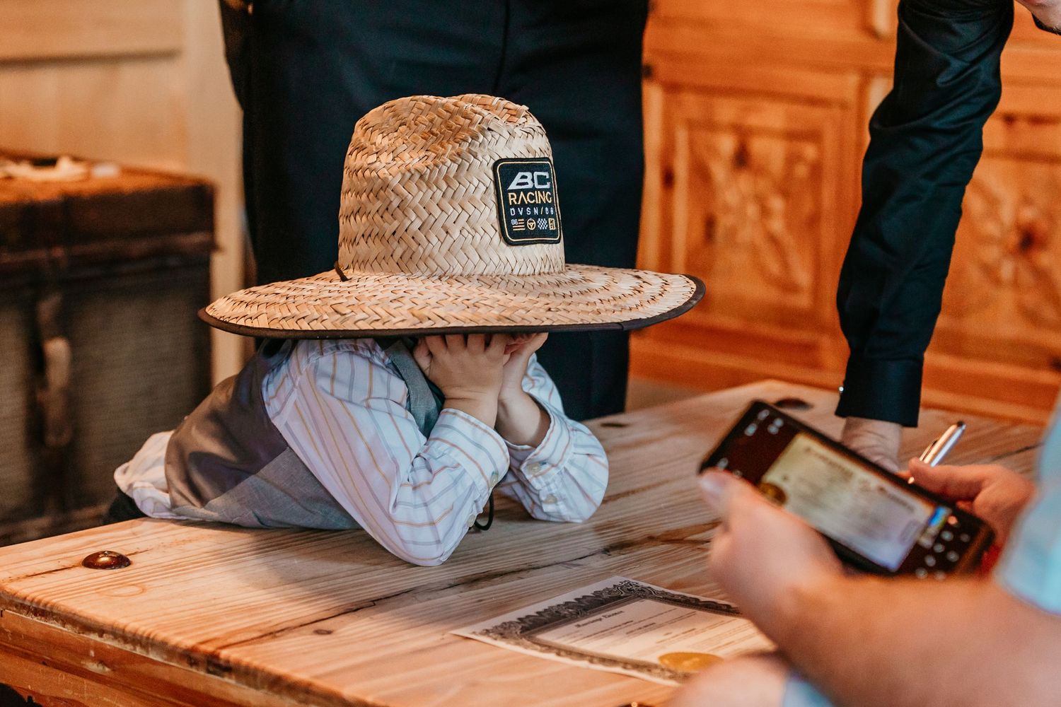 Wedding guests sign documents at a wooden table during the reception.