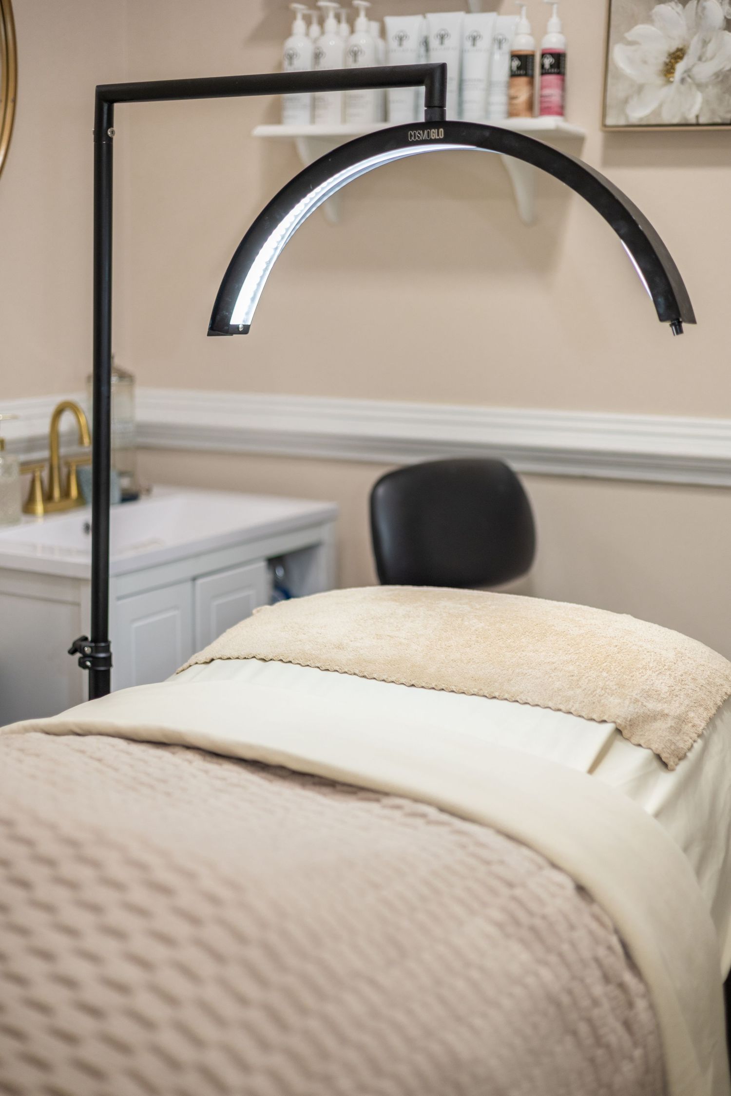 Elegant massage therapy room with white linens on treatment table and modern black lamp fixture overhead.
