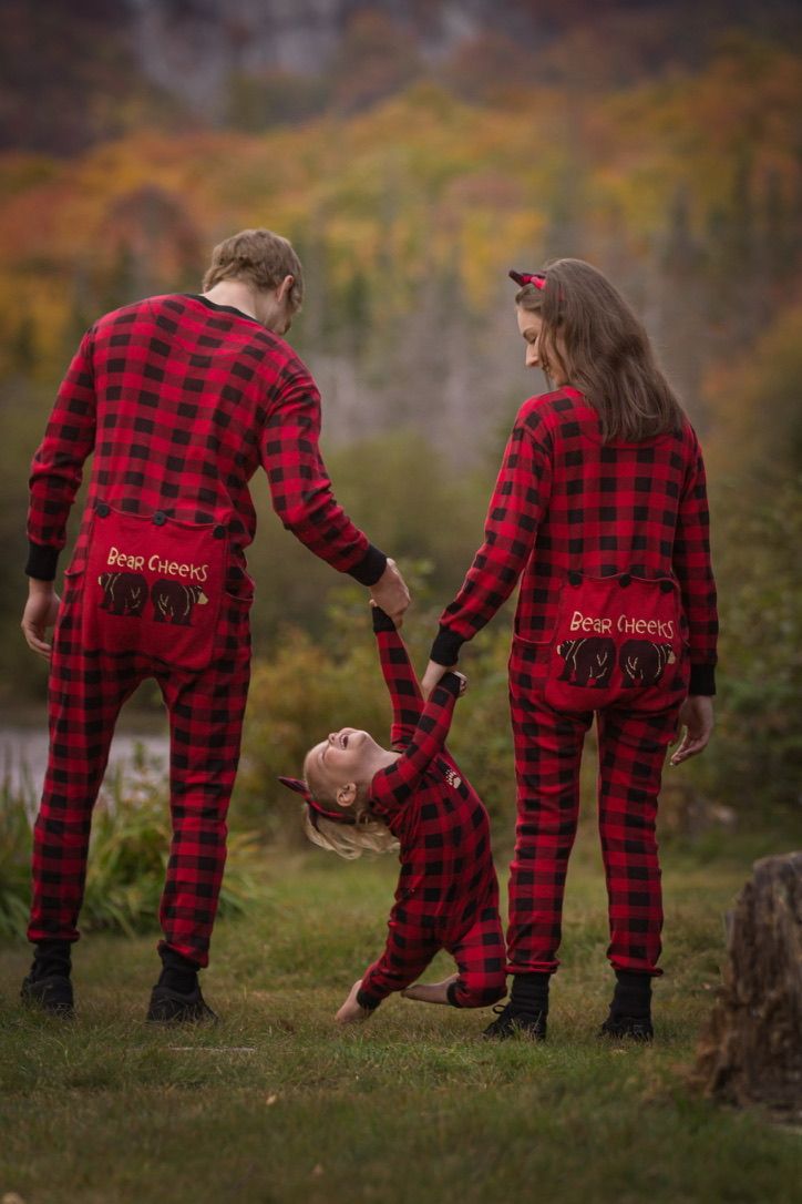Family wearing matching red buffalo plaid pajamas bending over in autumn setting.