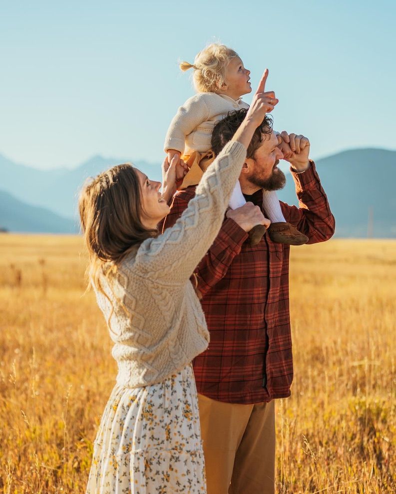 Family poses together in golden field with mountains in background.