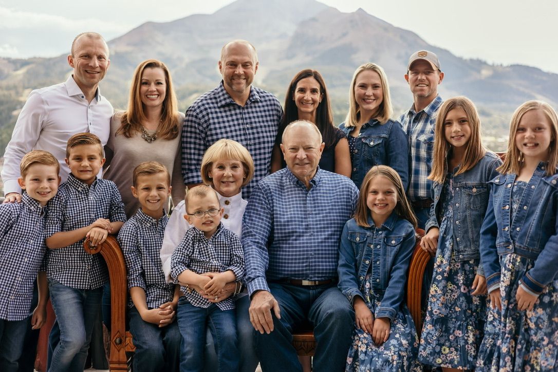 Multi-generational family portrait with mountain backdrop in coordinated blue and neutral outfits.