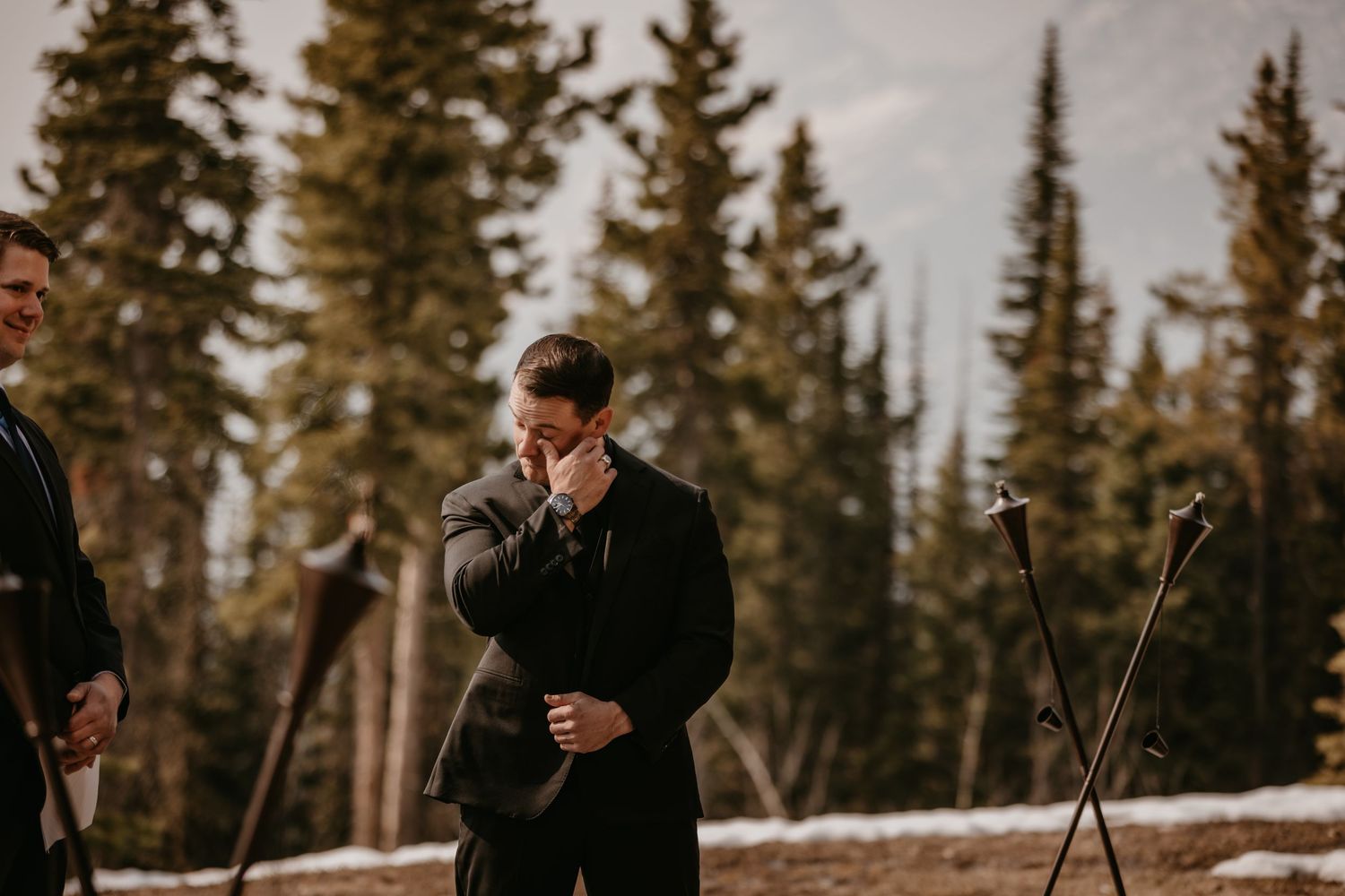 A winter wedding ceremony takes place in a snowy forest setting with evergreen trees in the background.