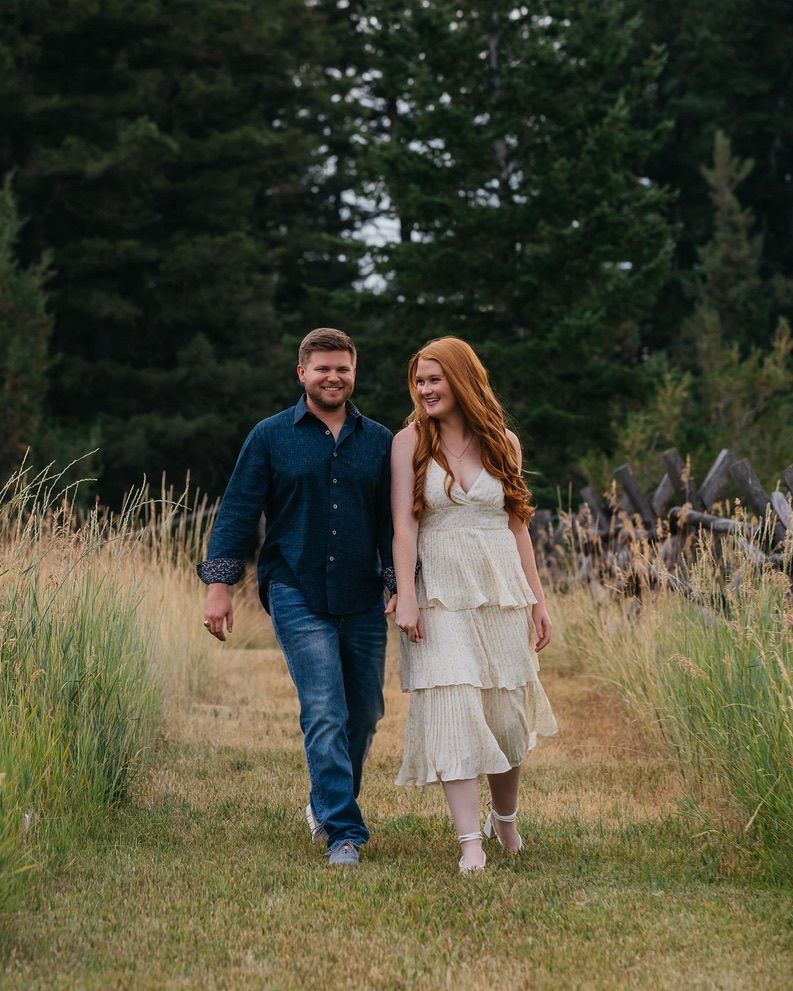 Couple walking through tall grass field during outdoor photoshoot.