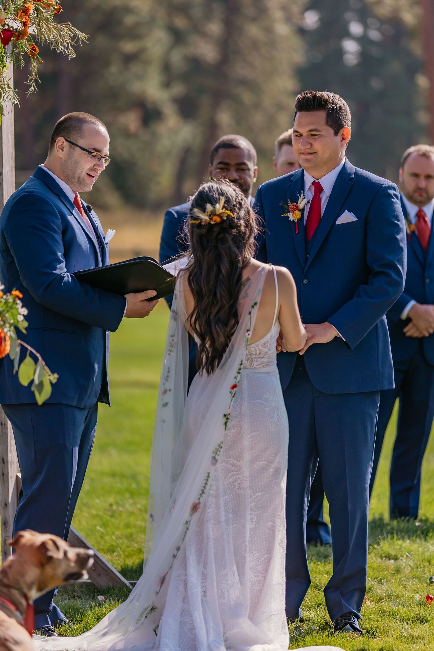 Wedding party in navy blue suits and white dresses gathered on sunny lawn.