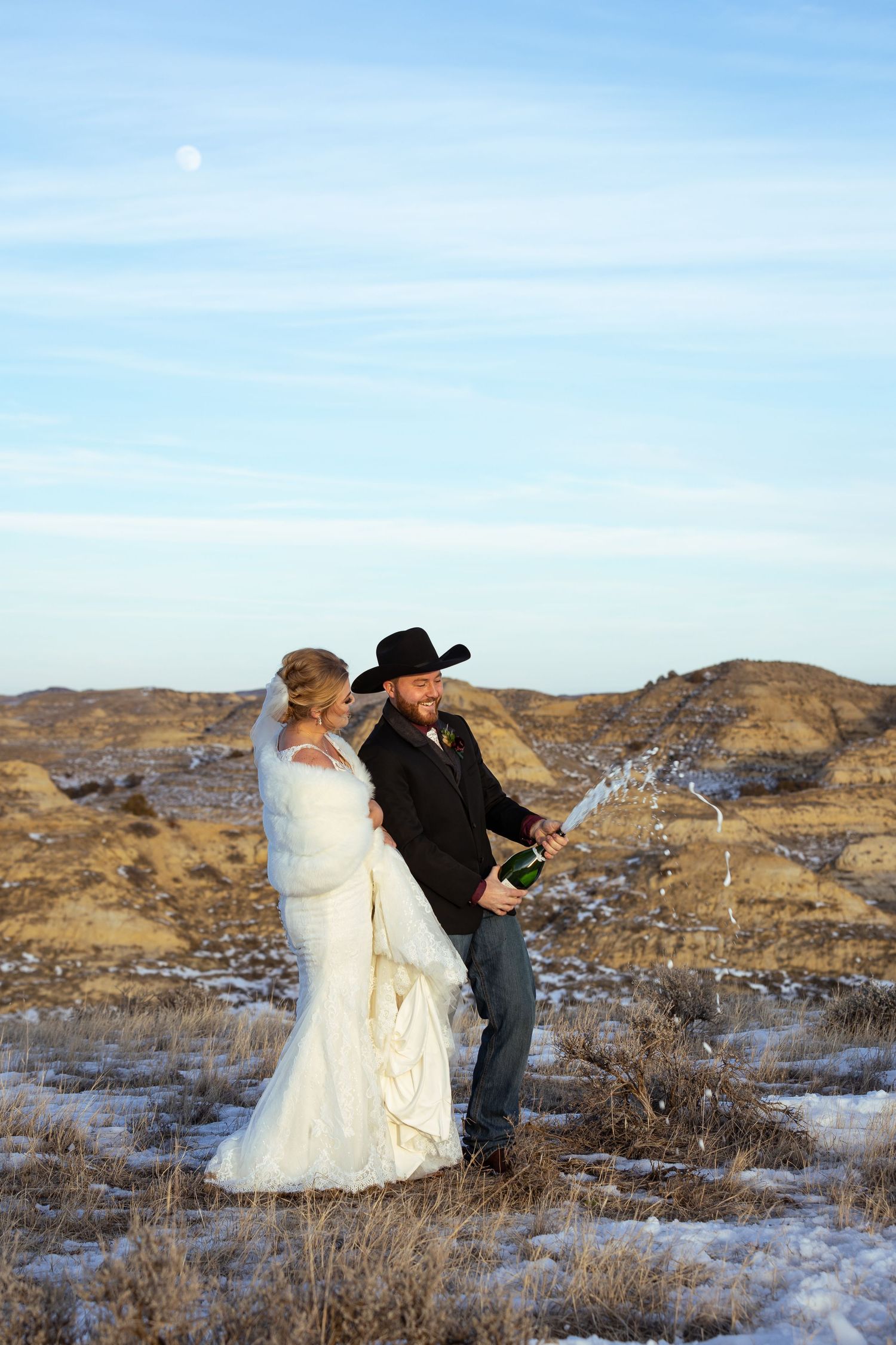 Wedding couple popping champagne in a snowy desert landscape at sunset.