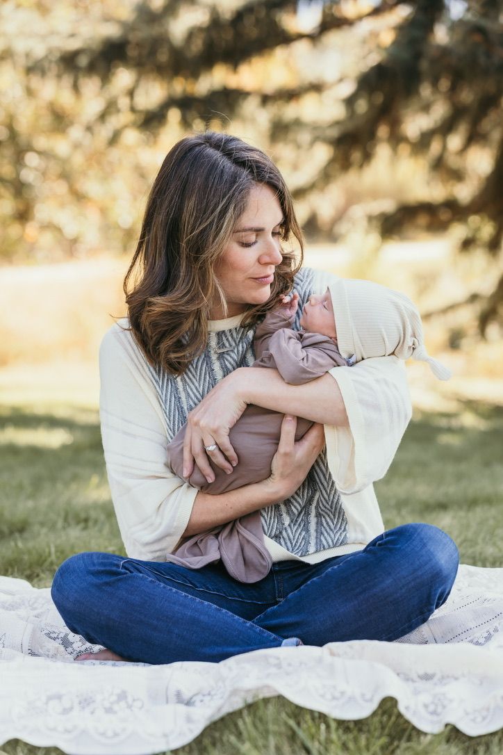 A tender moment on a blanket outdoors with a swaddled infant.
