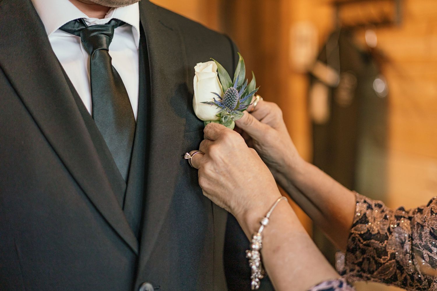 Detail shots of formal attire and boutonniere being pinned on black suit.