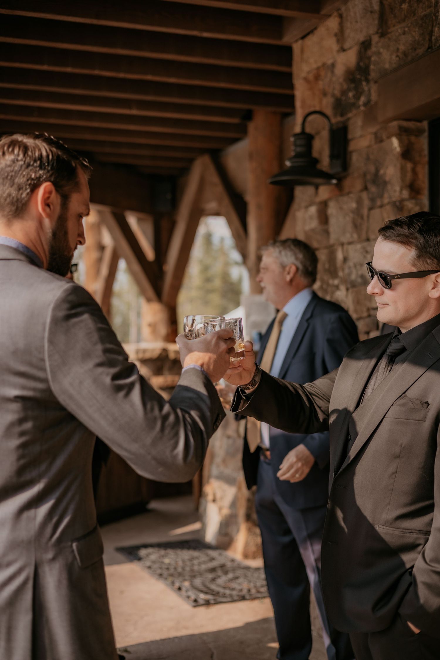 Wedding party members in dark suits celebrate with drinks under a covered patio.