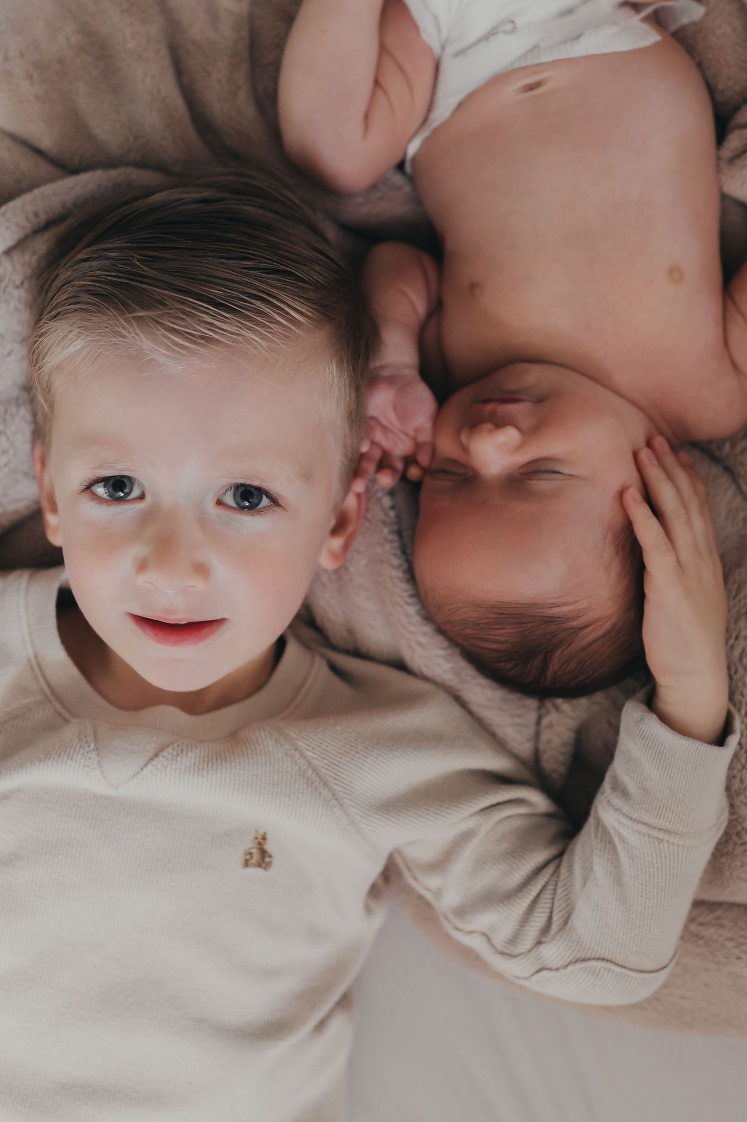 Close-up portrait of baby in beige clothing lying on soft surface.