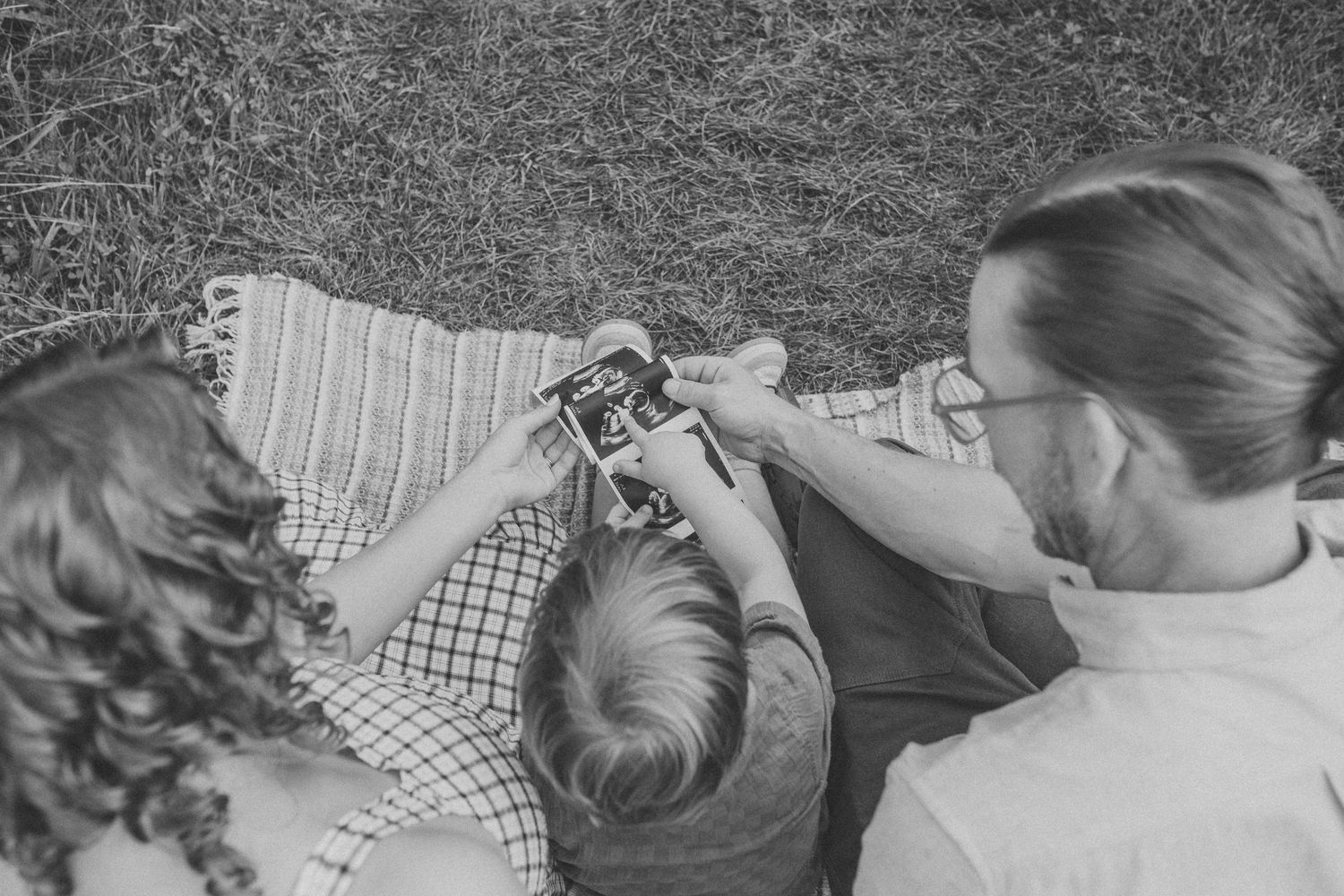 Black and white photo of a family sharing intimate moments on a blanket outdoors.