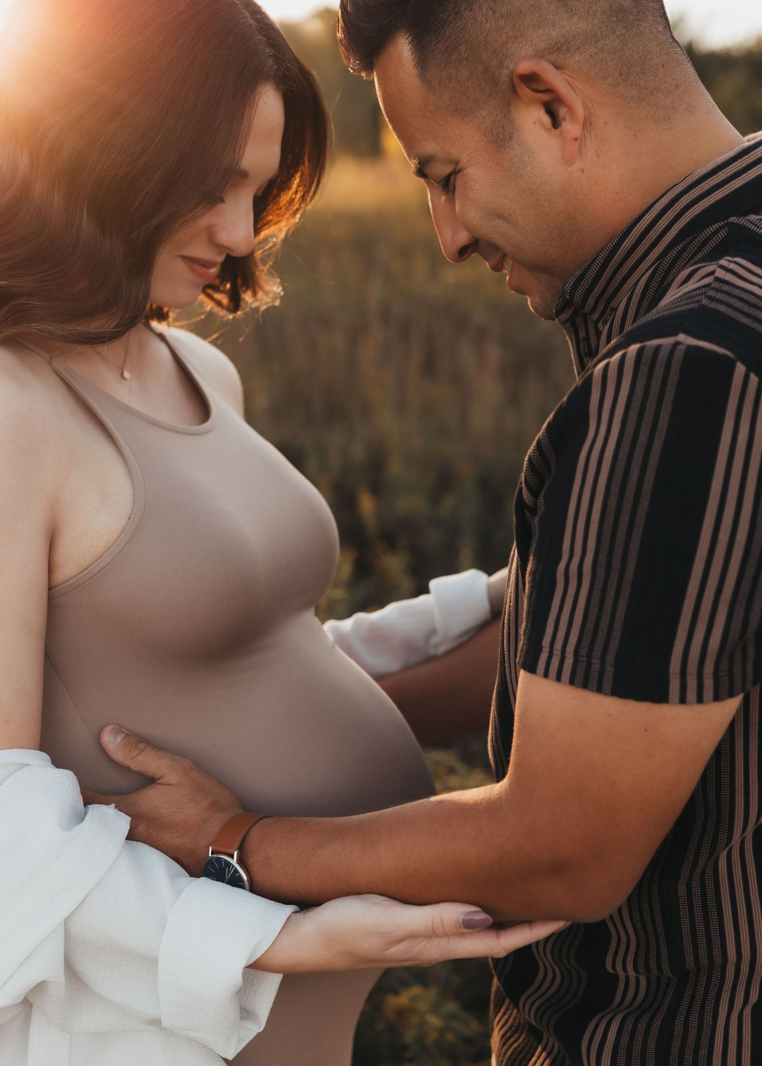 A couple in casual attire share an intimate moment during a golden hour photoshoot outdoors.