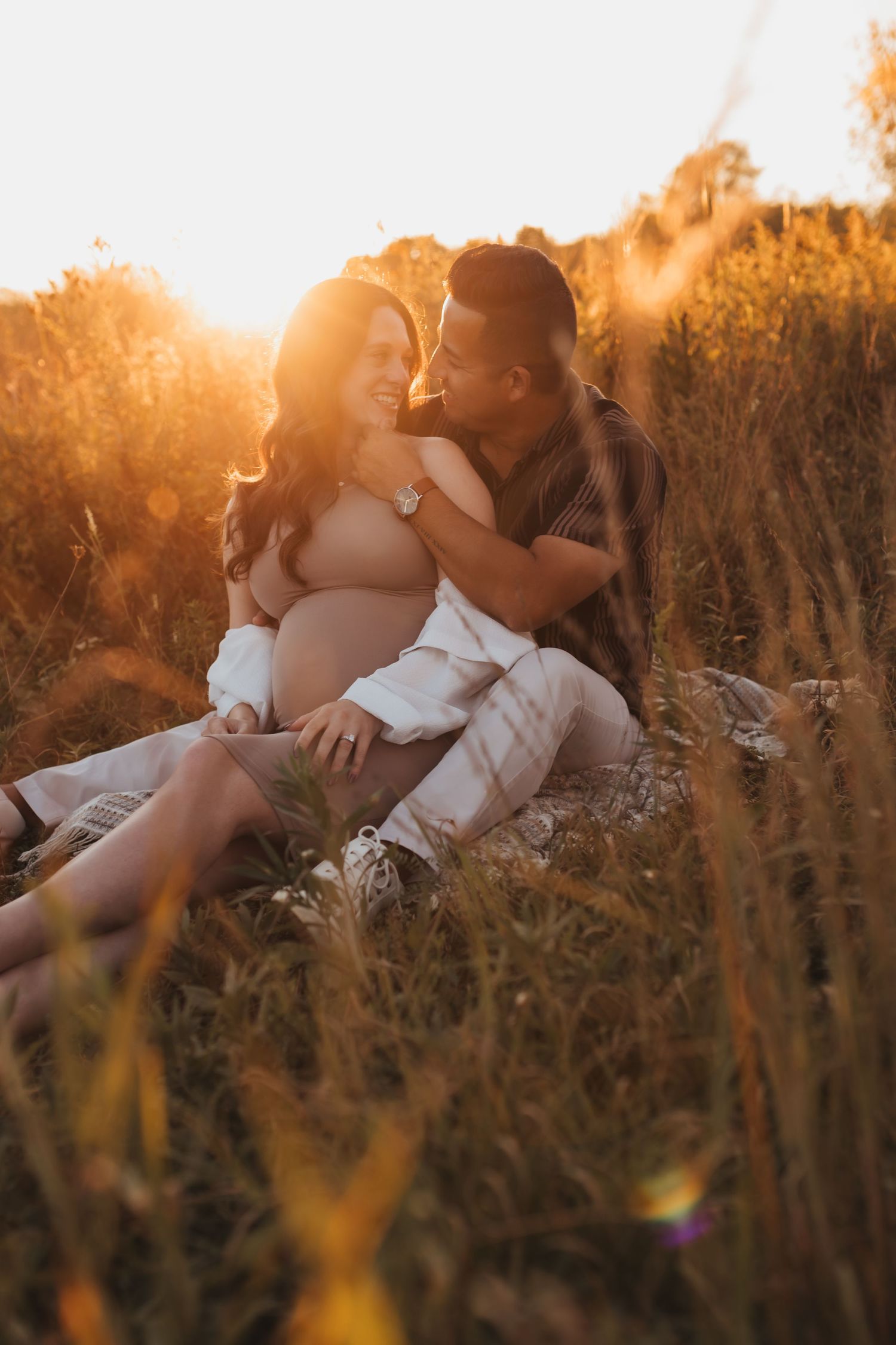 A romantic couple embraces in a golden field at sunset during a maternity photoshoot in nature.